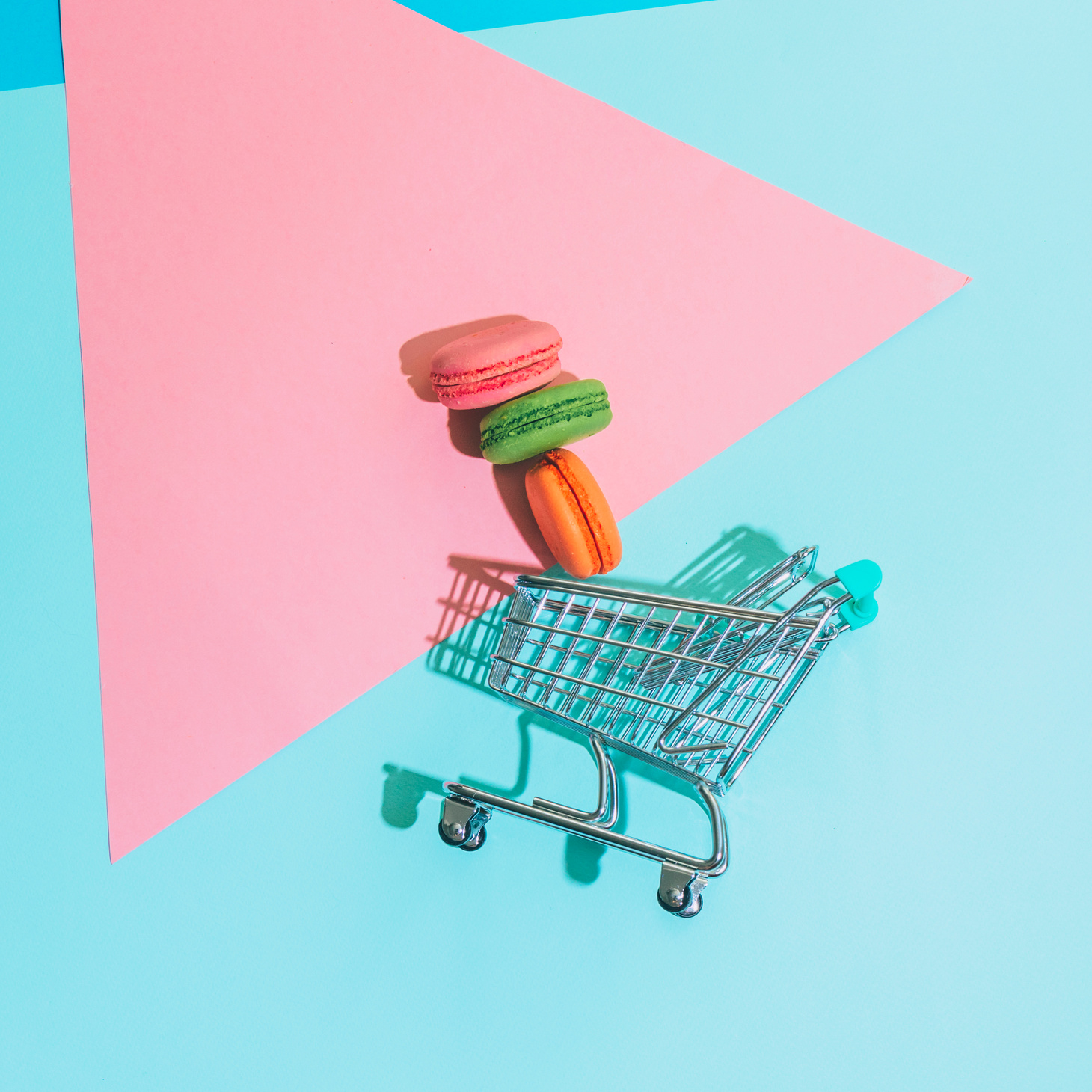 Colorful almond cookies macarons or macaroons fall from shopping cart on memphis style background.