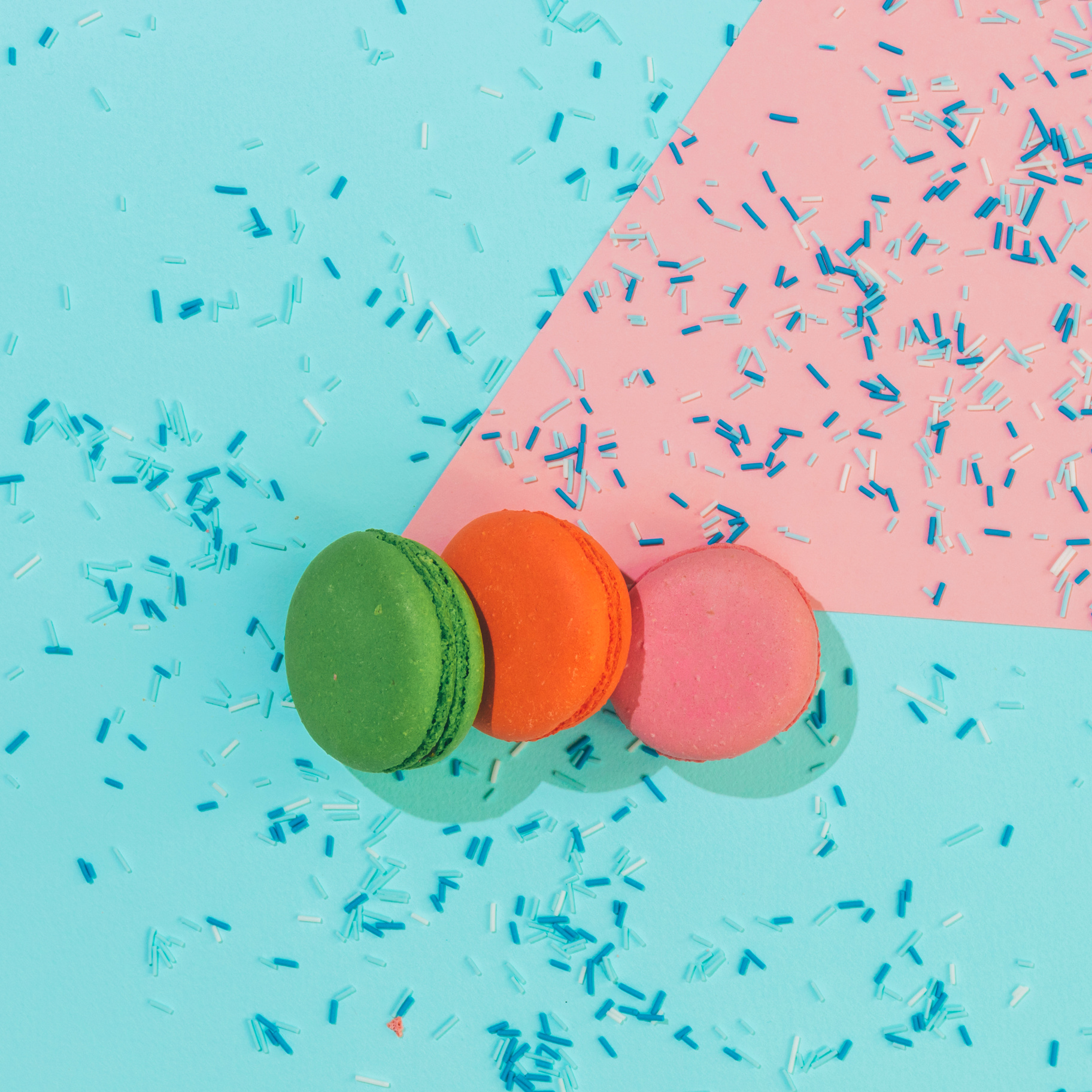 Stack of colorful almond macaroons or cookies with confetti on pink and blue background.